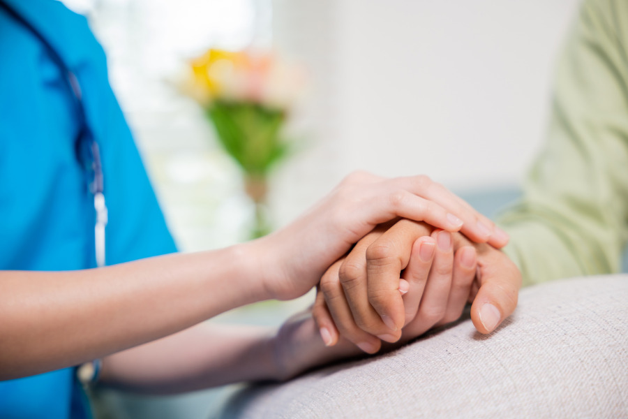 A burse holding the hand of a Burtonsville, MD patient in their home.