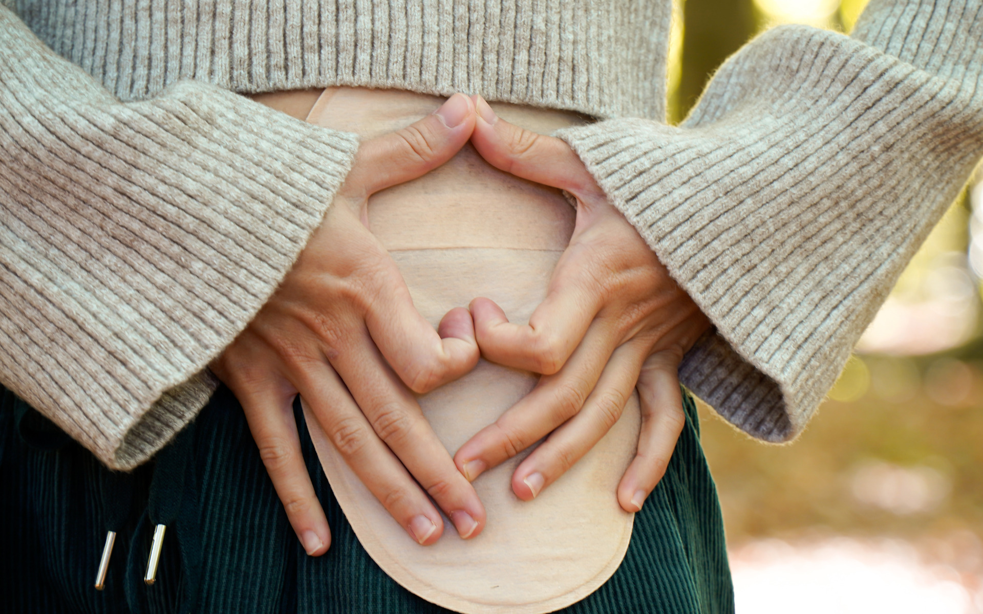 A person making a heart shape with their hands over their ostomy bag.